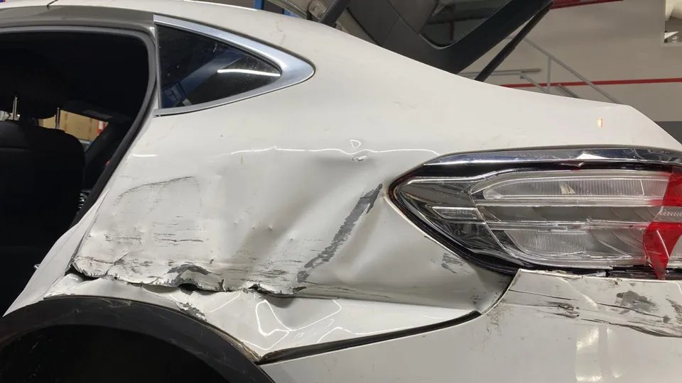 Beschädigte hintere Seitenwand eines weißen Mercedes in der AMK-Werkstatt